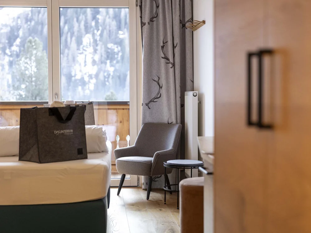 Interno di una stanza d'albergo con poltrona grigia e finestra con vista montagna