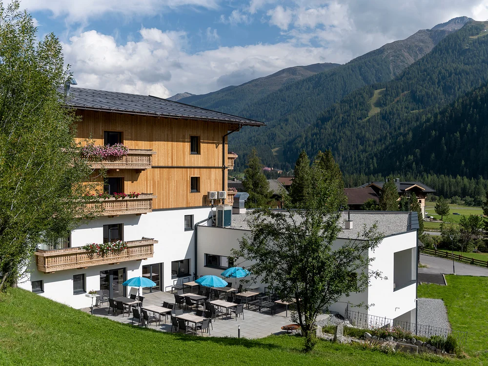 Hotel con terrazza e ombrelloni blu vicino a montagne verdeggianti