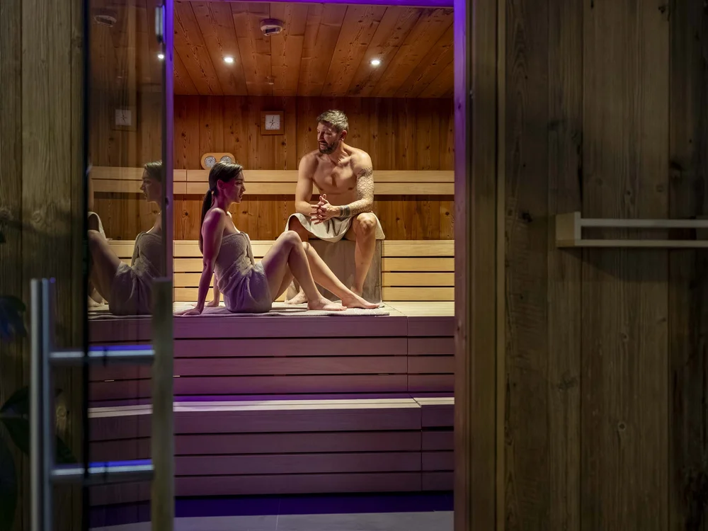 Coppia rilassata seduta in sauna di legno con asciugamani