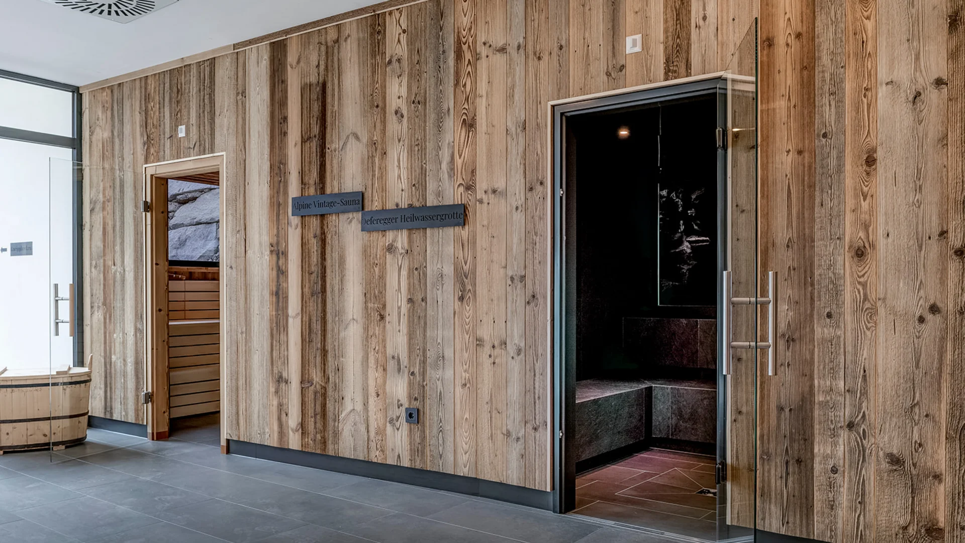 Parete in legno con ingresso a sauna e porta in vetro aperta