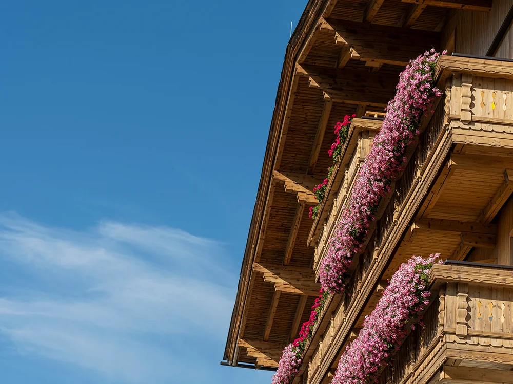 Balcone in legno decorato con fiori rosa sotto un cielo azzurro