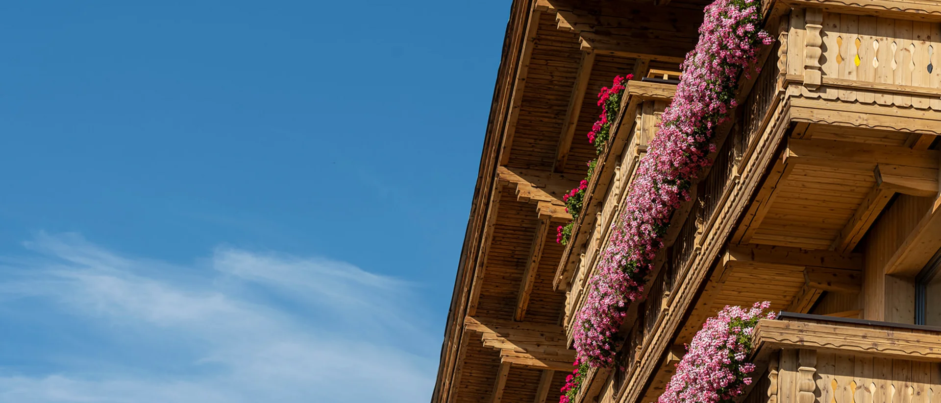 Balcone in legno decorato con fiori rosa sotto un cielo azzurro