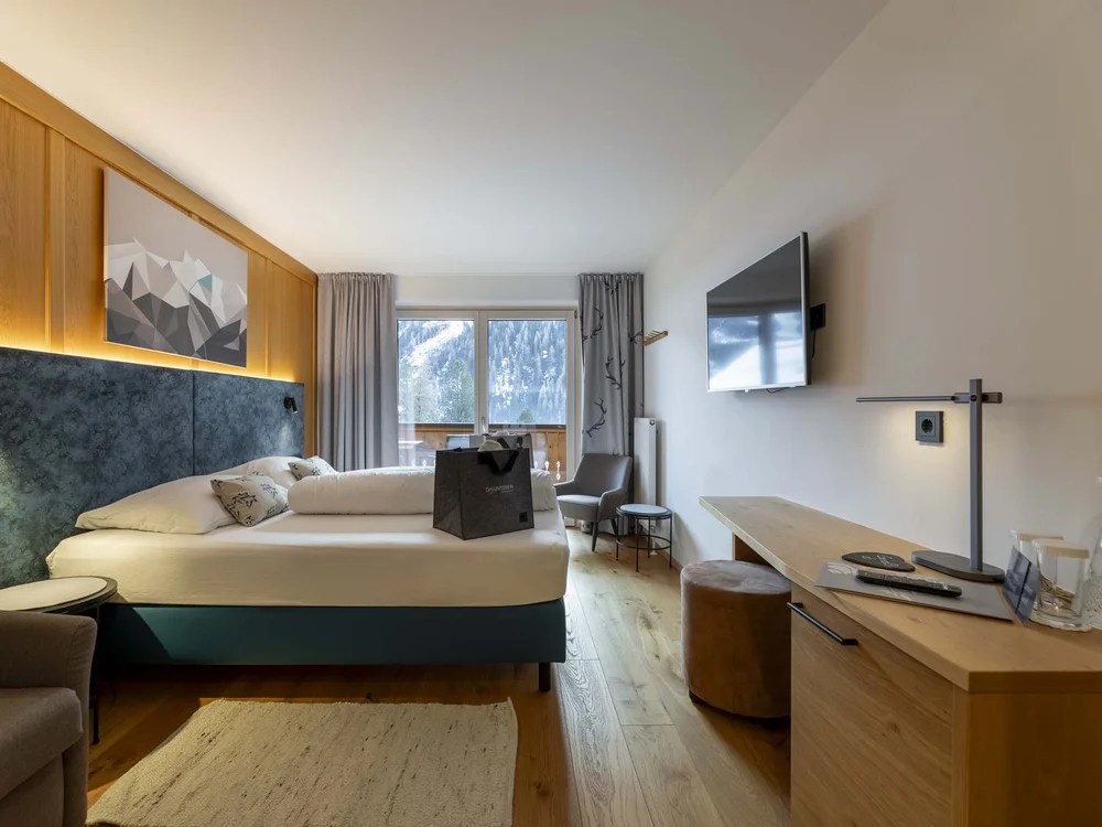Camera d'hotel moderna con letto, TV a parete e vista sulle montagne innevate