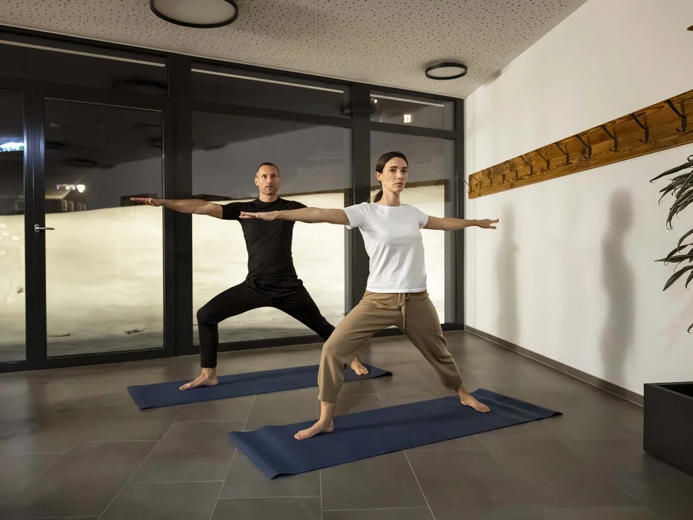 Due persone praticano yoga in una stanza luminosa con tappetini blu