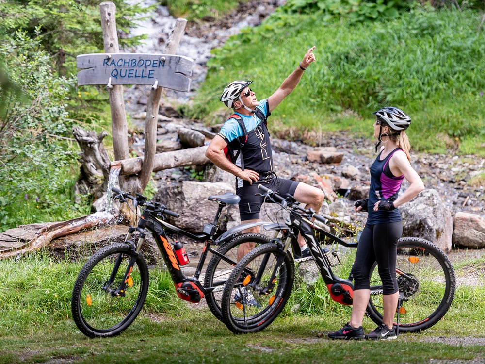 Due ciclisti si fermano vicino a un cartello in legno in un'area verde