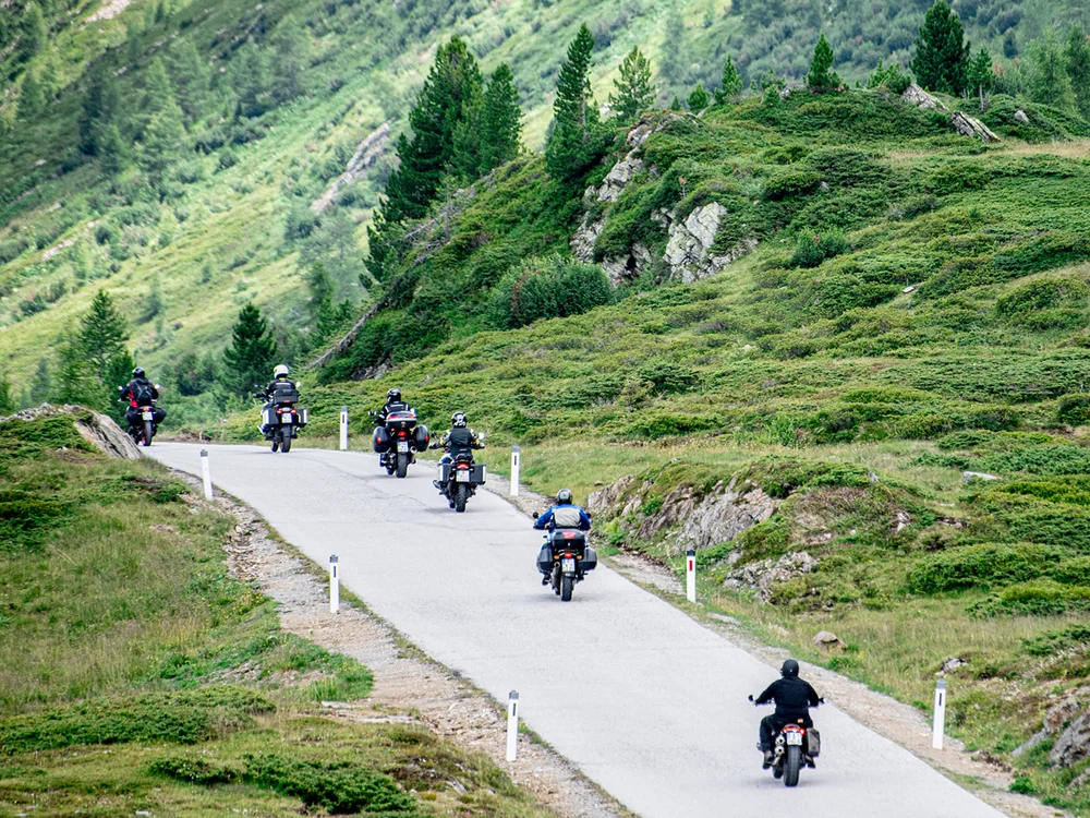 Gruppo di motociclisti che percorrono una strada di montagna verde e curva