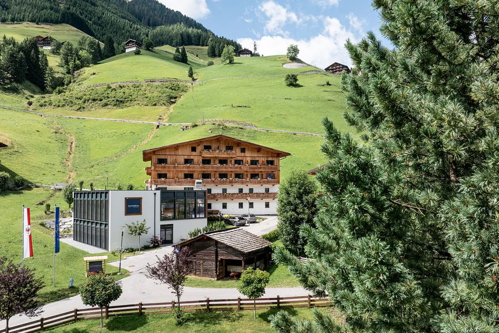 Hotel in legno con vista su colline verdi e alberi sotto un cielo parzialmente nuvoloso