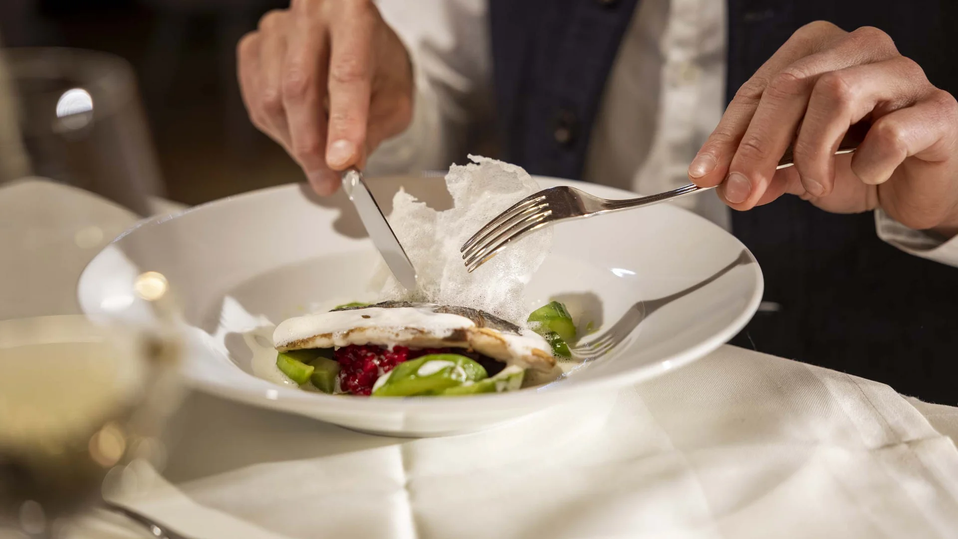 Persona che taglia il cibo con coltello e forchetta in un piatto elegante