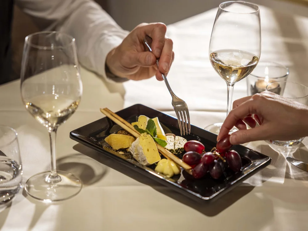 Piatto di formaggi, uva e grissini con calici di vino bianco
