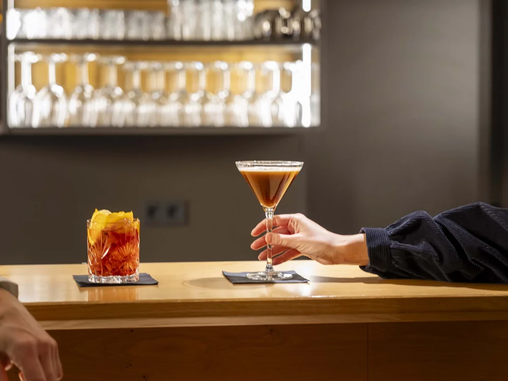 Brindisi con cocktail su un tavolo di legno in un bar moderno.