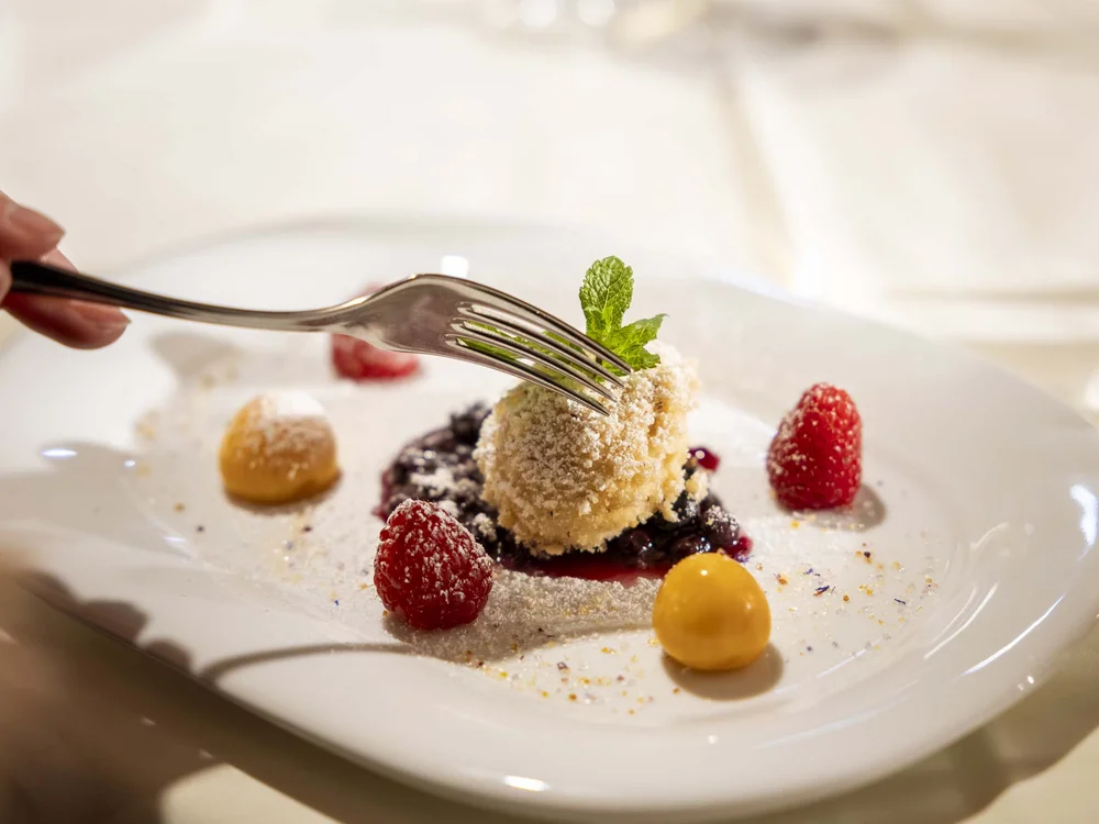 Forchetta che affetta un dessert con frutti di bosco e foglia di menta